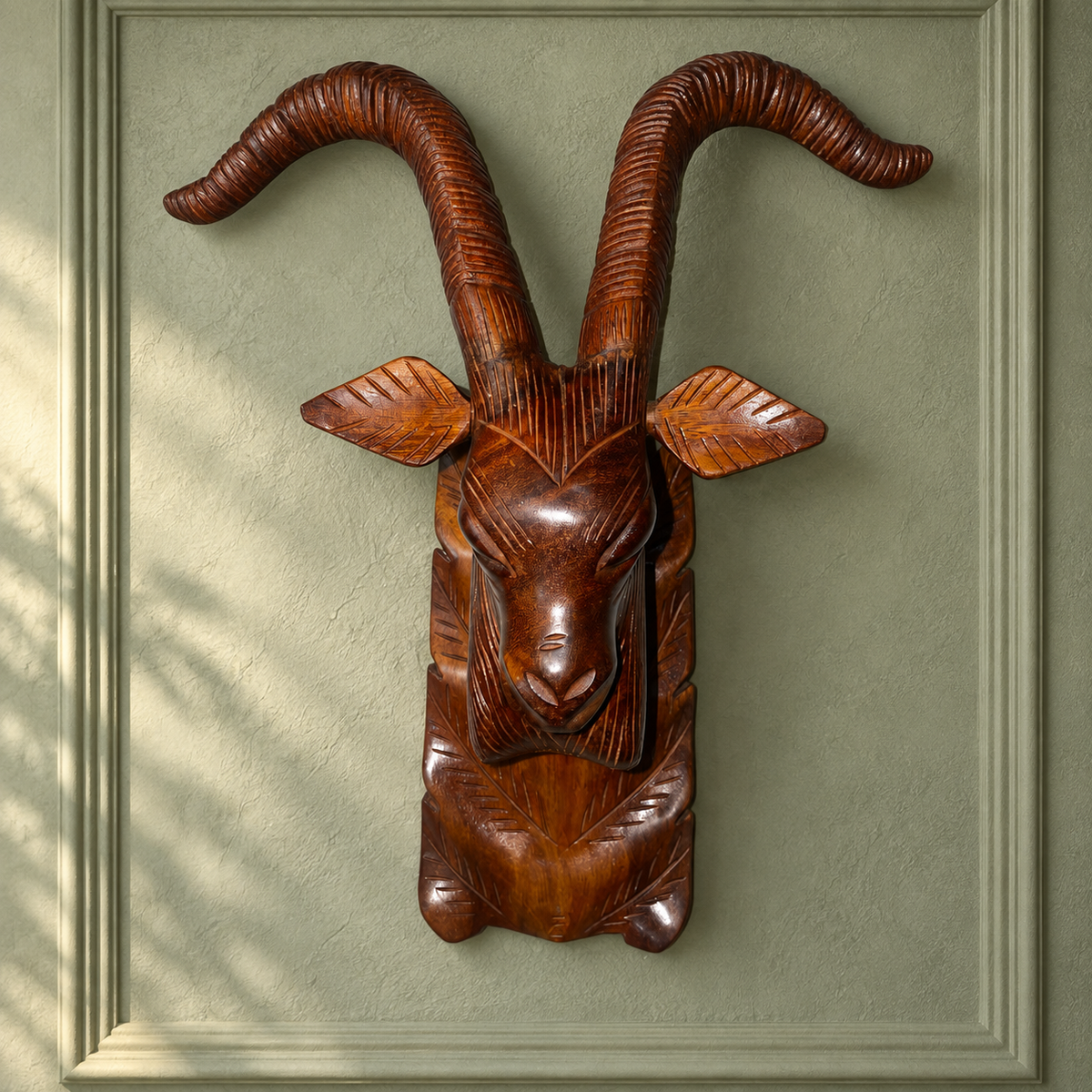 Carved wooden ibex head wall sculpture hanging on a sage green panelled wall